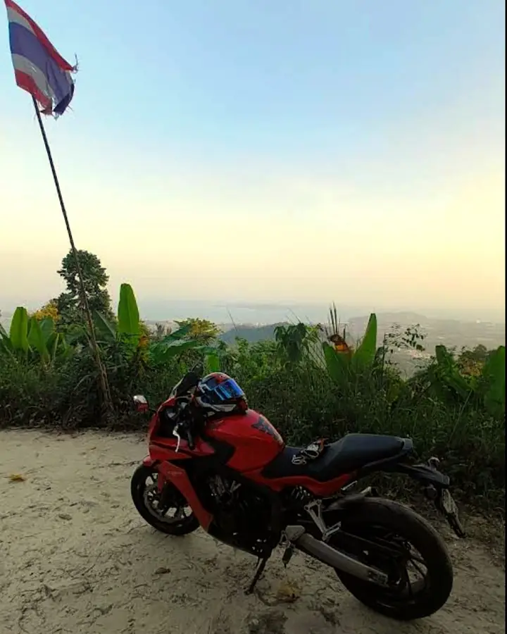 Red Honda next to a Thai flag on a hilltop